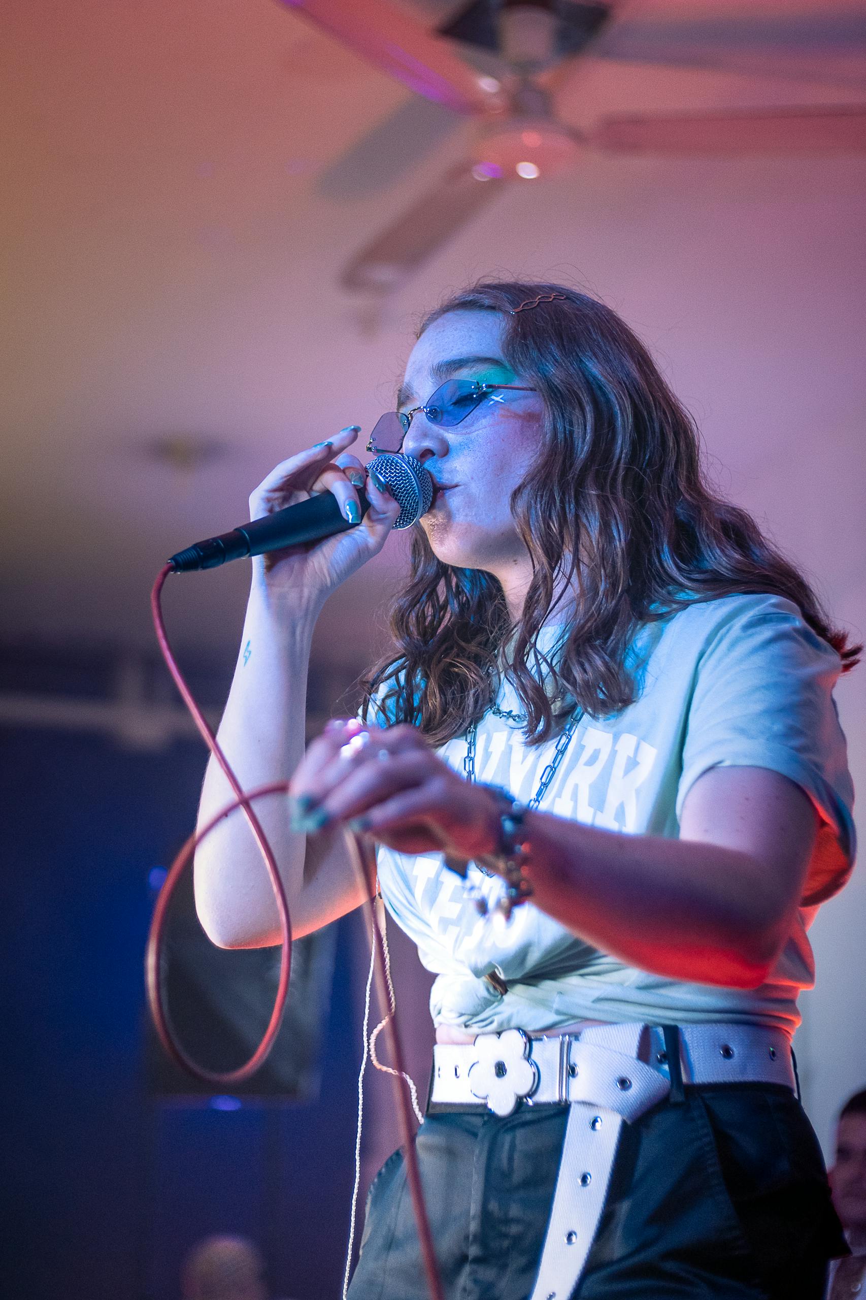 A female singer passionately performing on stage with a microphone in a vibrant setting.